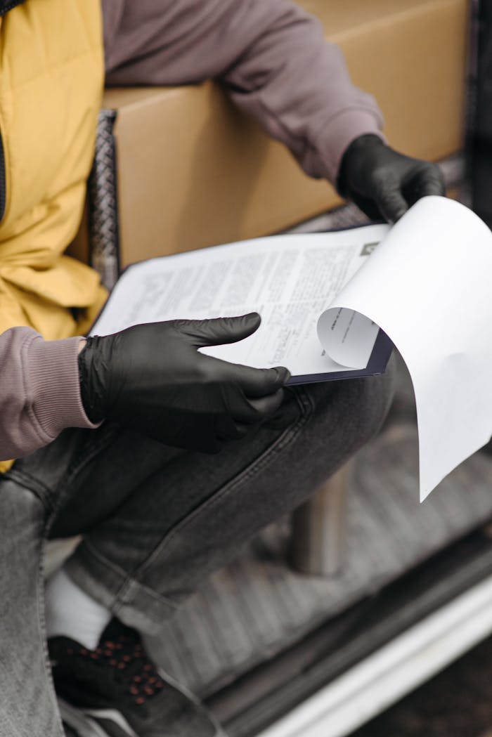 Courier with gloves reviewing delivery paperwork in vehicle interior.